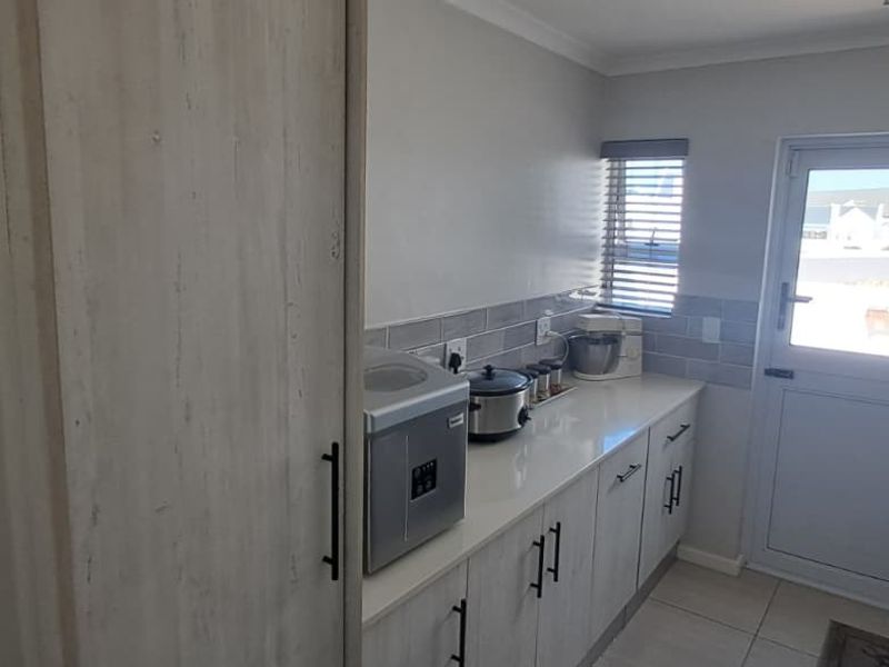 A functional scullery featuring modern built-in cabinetry, stone countertops, subway tile backsplash, and direct access to the exterior.