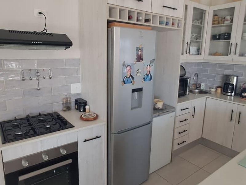 A well-appointed kitchen featuring light-toned cabinetry, stone countertops, a gas hob with extractor fan, and a stylish subway tile backsplash.