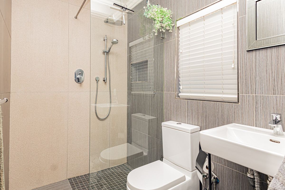 Modern bathroom featuring a glass-enclosed shower with a built-in niche, wall-mounted basin, and contemporary tiled finishes throughout.