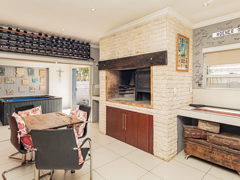 An enclosed entertainment area featuring a built-in braai with stone cladding, tiled flooring, and integrated wine storage, perfect for social gatherings.