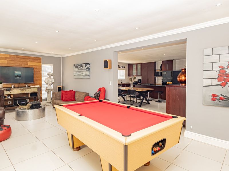 Spacious open-plan living area featuring a modern kitchen with dark cabinetry, tiled floors, and recessed lighting, seamlessly flowing into a versatile entertainment space.