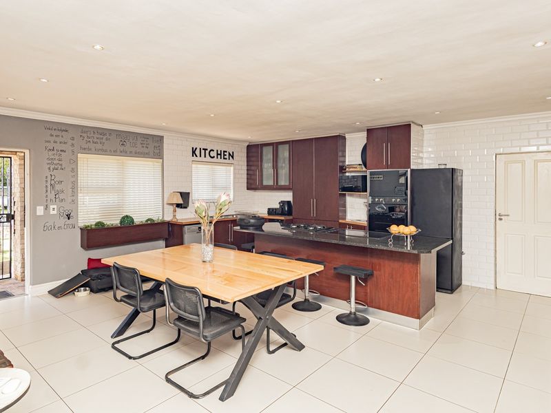 Spacious open-plan kitchen and dining area featuring dark wood cabinetry, granite countertops, subway tile backsplash, and modern recessed lighting.