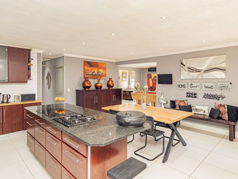 Spacious open-plan kitchen and dining area featuring a large granite island with integrated gas hob, modern cabinetry, and neutral tiled flooring throughout.