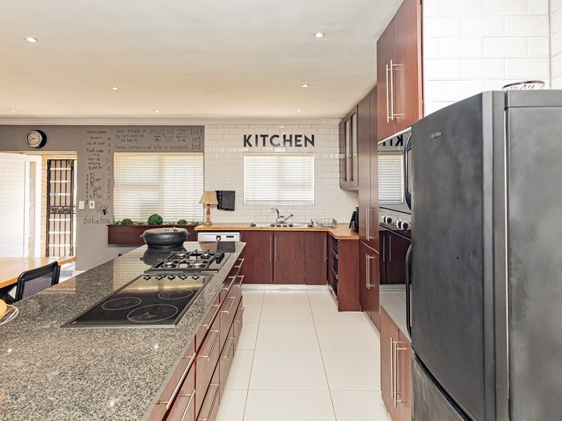 Modern kitchen featuring a large granite-topped island with dual hobs, ample dark wood cabinetry, subway tile backsplash, and recessed lighting.