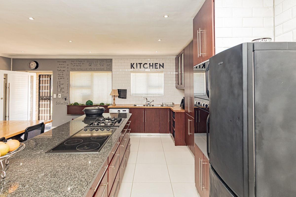 Modern kitchen featuring a large granite-topped island with dual hobs, ample dark wood cabinetry, subway tile backsplash, and recessed lighting.