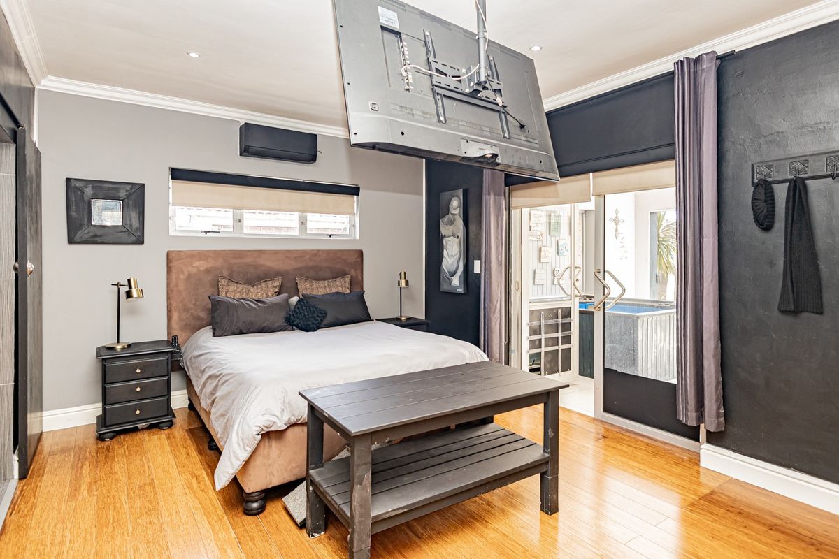 Spacious bedroom featuring hardwood flooring, recessed lighting, a wall-mounted air conditioning unit, and direct access to an outdoor area through sliding glass doors.