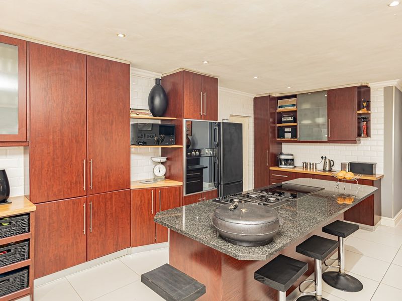 Spacious kitchen featuring dark wood cabinetry, granite countertops, a central island with a gas hob, and modern subway tile backsplash.