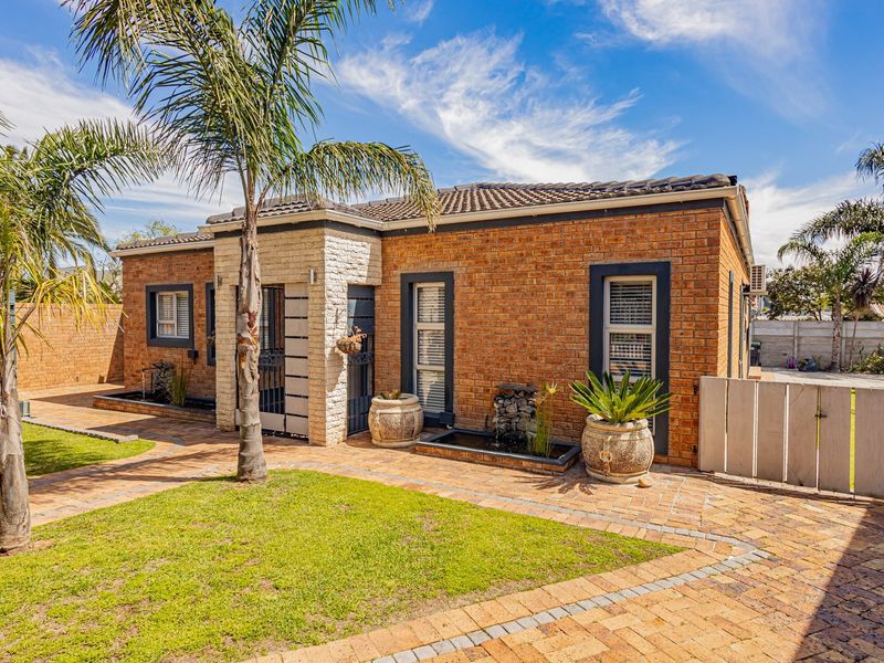 A well-maintained face brick home featuring stone cladding accents, a paved driveway, and a landscaped front garden with a built-in water feature.