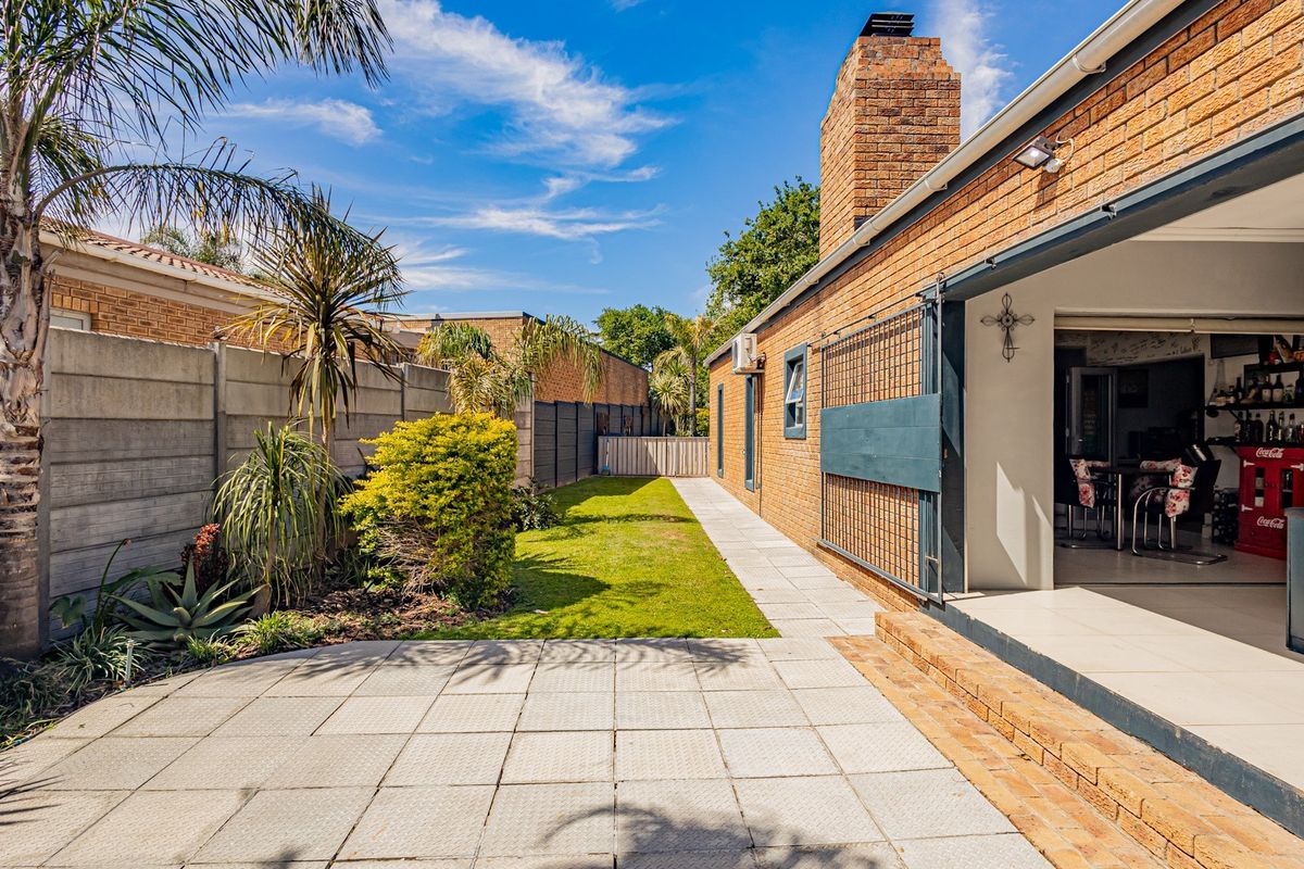 Rear exterior view featuring a paved patio area, brick facade, chimney, and a well-maintained garden with a boundary wall.