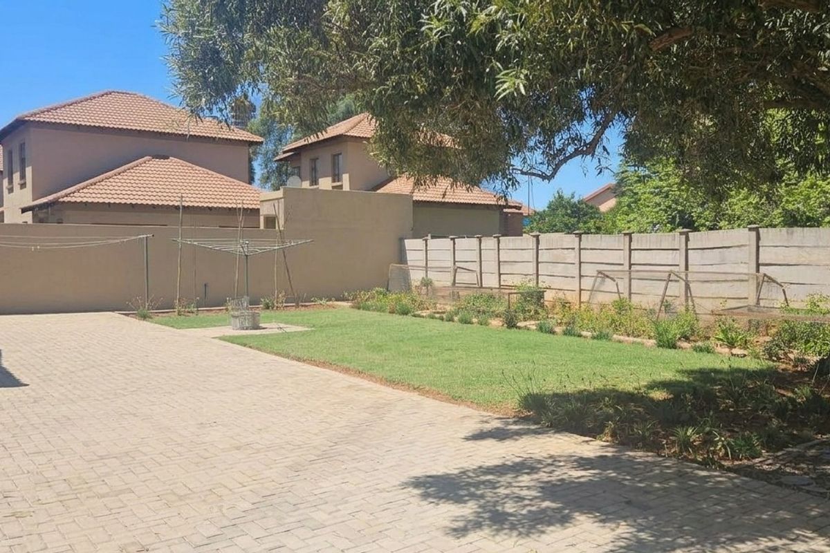 A spacious rear garden featuring a paved driveway, a well-maintained lawn, and a secure perimeter wall.