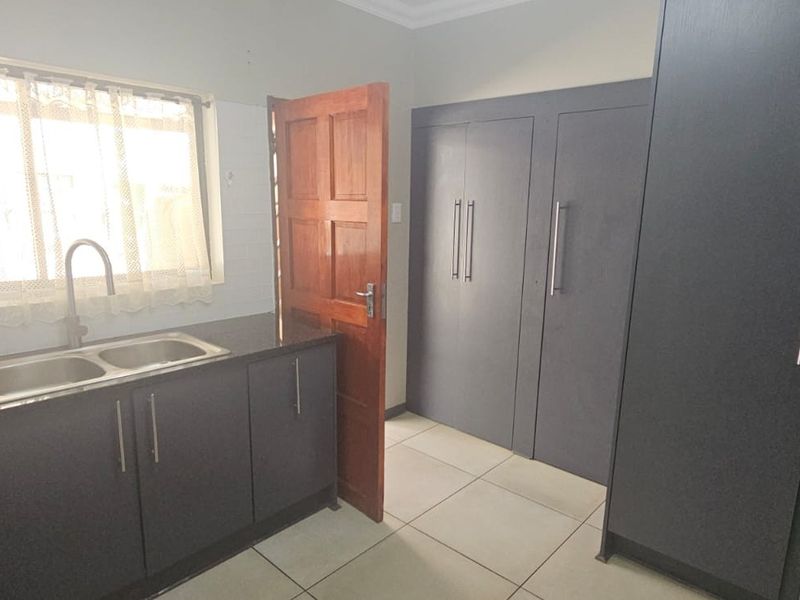 A clean, modern kitchen featuring dark grey cabinetry, granite countertops, a double bowl sink, and ample built-in storage space with tiled flooring.