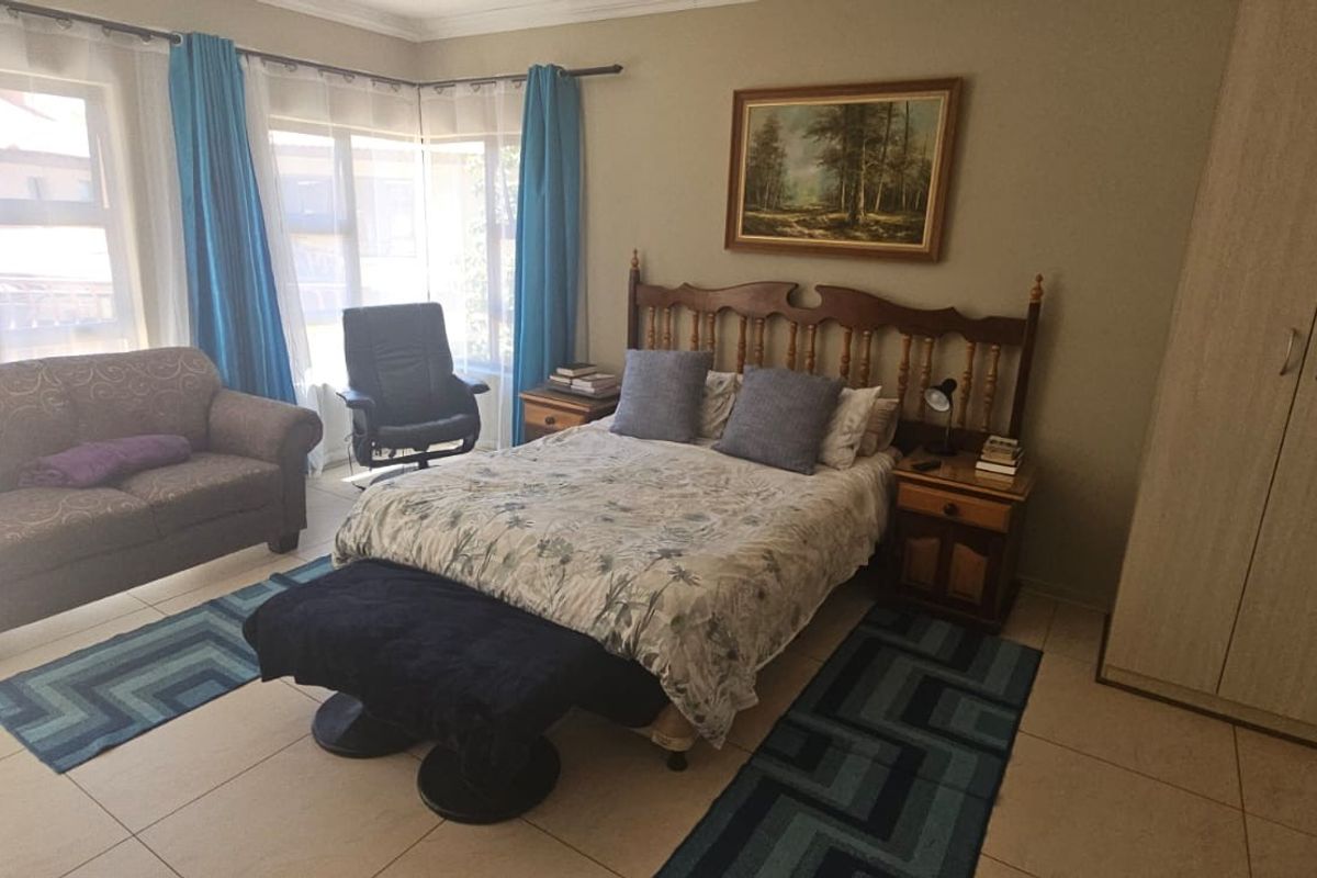 A spacious bedroom featuring tiled flooring, a large built-in wardrobe, and ample natural light from the corner windows.