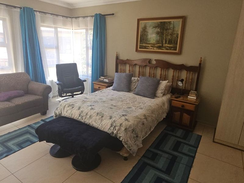 A spacious bedroom featuring tiled flooring, a large built-in wardrobe, and ample natural light from the corner windows.