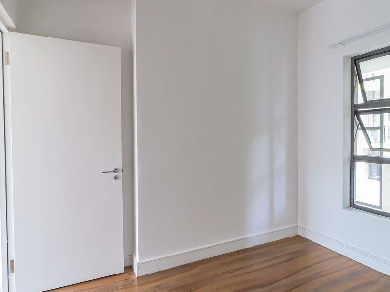 A bright, empty bedroom featuring laminate flooring, clean white walls, and an aluminium-framed window.