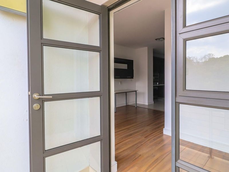 View through an open aluminium framed glass door into an empty living area featuring modern laminate flooring.