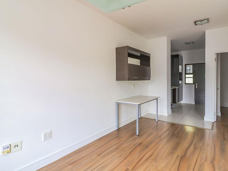 An open-plan living area featuring a mix of laminate and tiled flooring, with a wall-mounted storage unit and neutral finishes throughout.