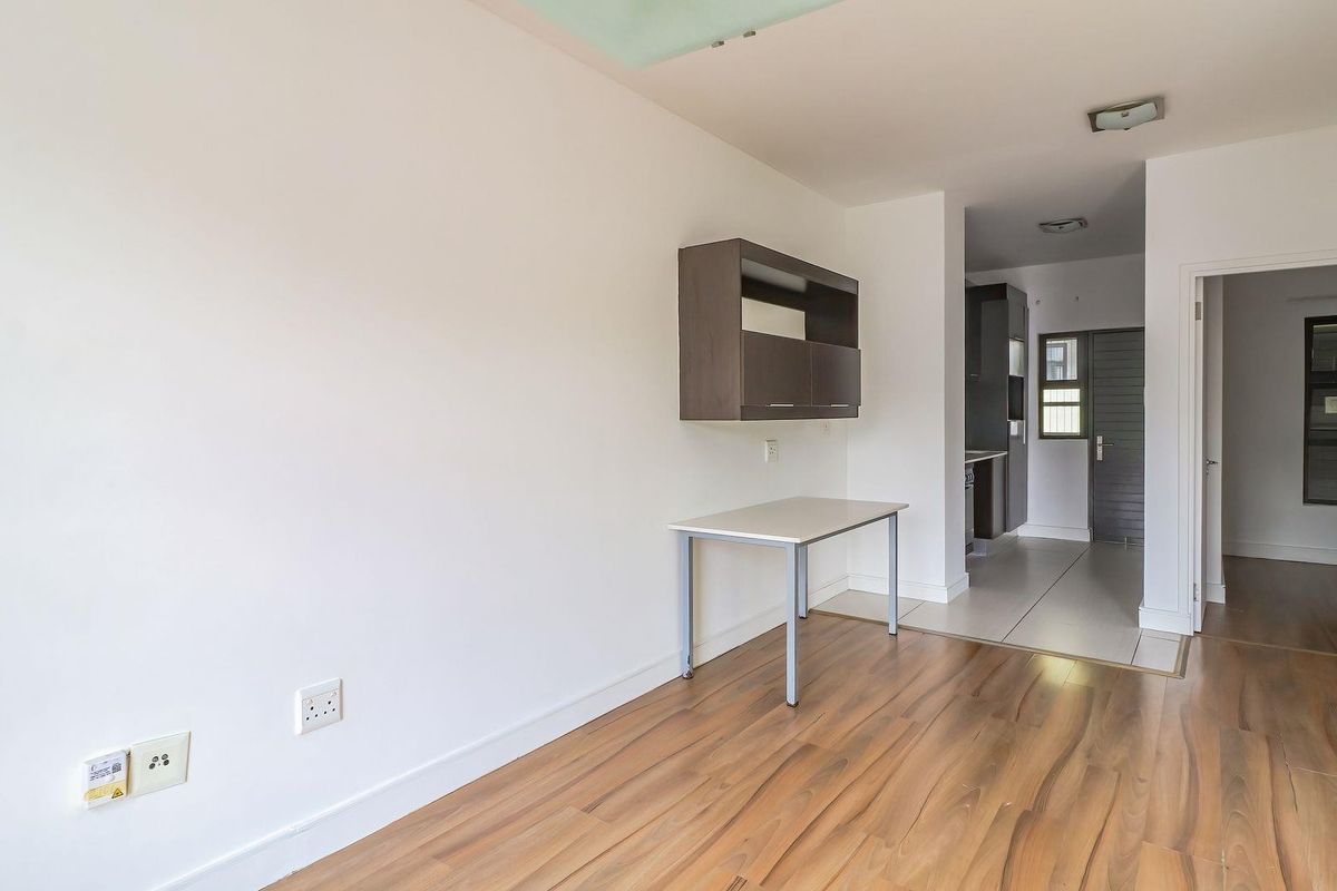 An open-plan living area featuring a mix of laminate and tiled flooring, with a wall-mounted storage unit and neutral finishes throughout.
