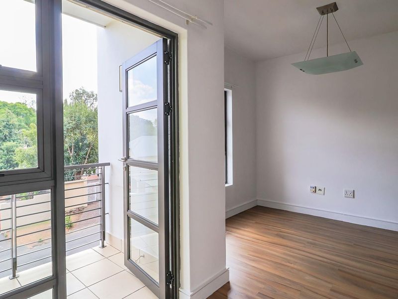Bright living area featuring laminate flooring, a modern pendant light, and direct access to a private balcony through large glass doors.