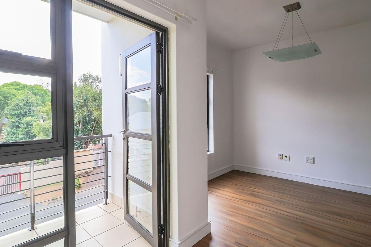 Bright living area featuring laminate flooring, a modern pendant light, and direct access to a private balcony through large glass doors.