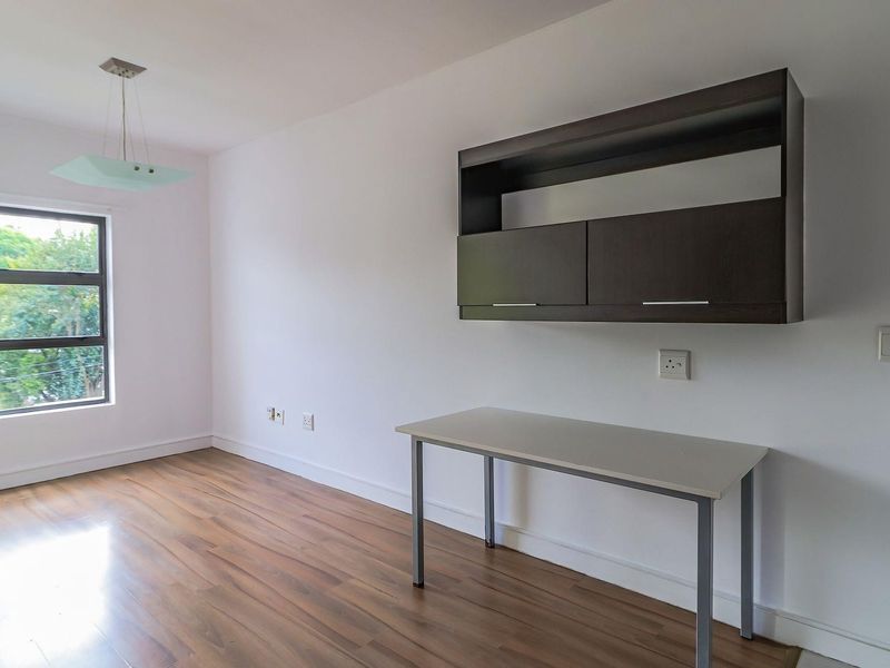 A bright, empty bedroom featuring laminate flooring, a built-in wall cabinet, and a large window providing natural light.