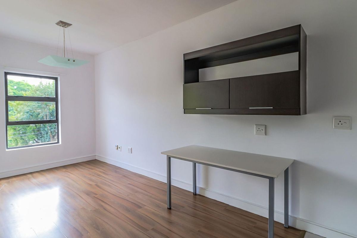 A bright, empty bedroom featuring laminate flooring, a built-in wall cabinet, and a large window providing natural light.