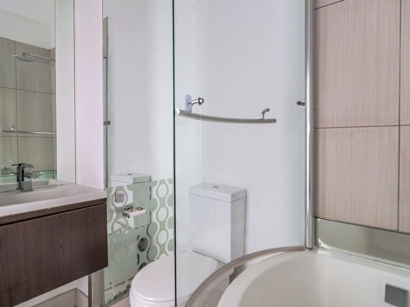 A modern bathroom featuring a vanity with basin, a toilet, and a glass-enclosed shower with neutral wall tiling.