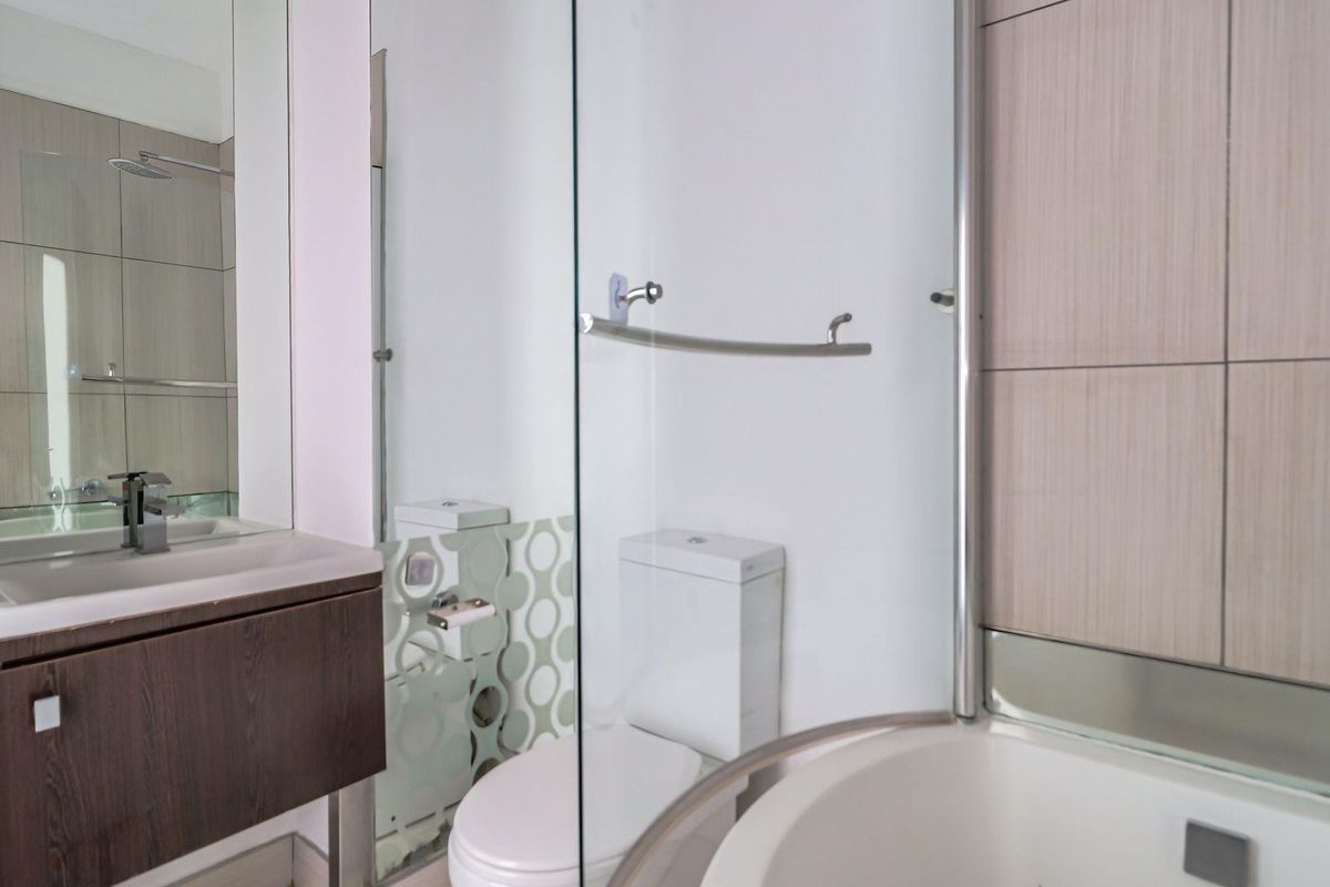 A modern bathroom featuring a vanity with basin, a toilet, and a glass-enclosed shower with neutral wall tiling.