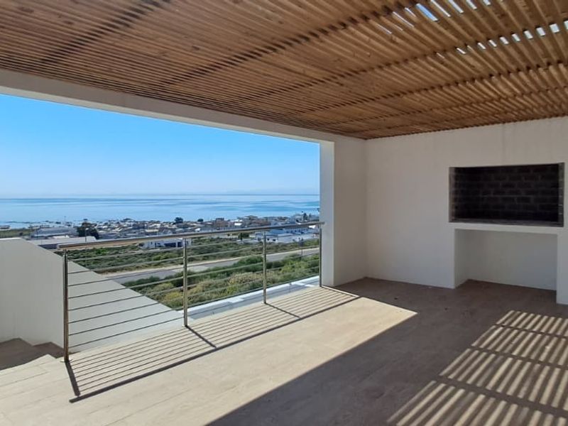 Spacious covered balcony featuring a timber slat ceiling, built-in braai, and stainless steel balustrade, offering expansive coastal and ocean views.