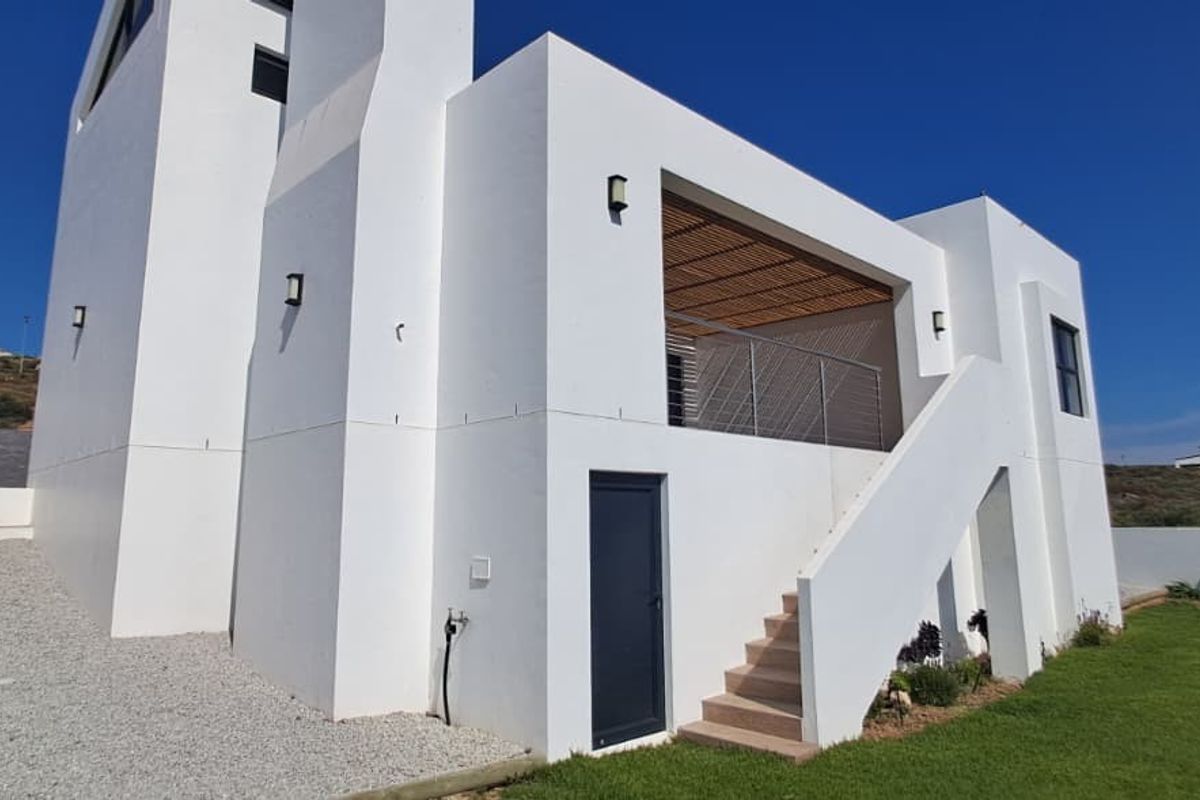 Modern white exterior featuring a covered balcony, external staircase, and well-maintained lawn area.