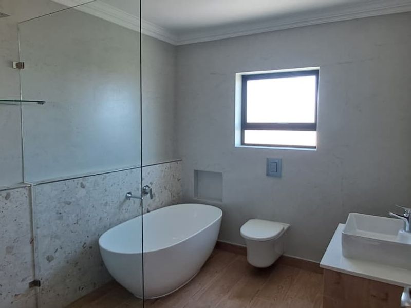 Modern bathroom featuring a sleek freestanding bathtub, wall-mounted toilet, vanity basin, and a spacious walk-in shower with a rain shower head.