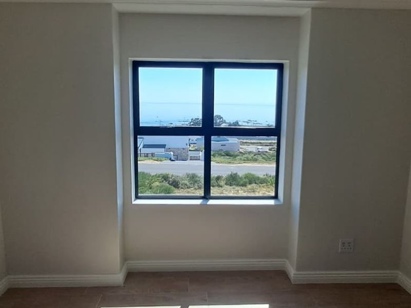 A bright, empty bedroom featuring tiled flooring, neutral walls, and a large window offering scenic coastal views.