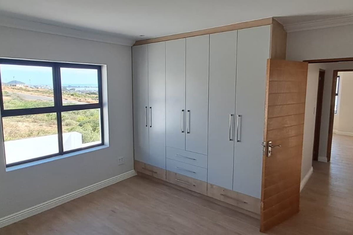 A bright, modern bedroom featuring built-in cupboards, light laminate flooring, and a window with a scenic view.