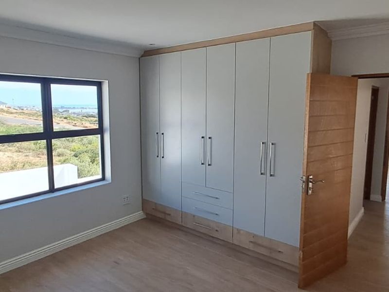 A bright, modern bedroom featuring built-in cupboards, light laminate flooring, and a window with a scenic view.