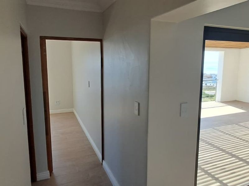 A bright, modern hallway featuring tiled flooring, wooden door frames, and large sliding glass doors leading to an outdoor patio area.