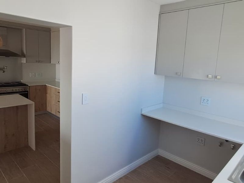 A clean, modern scullery area featuring ample built-in cabinetry, stone countertops, and a double sink, with a view into the adjacent kitchen.