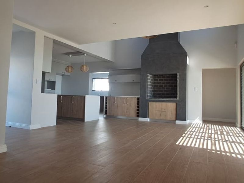 Spacious open-plan living area featuring wood-look tile flooring, a modern built-in fireplace, and a contemporary kitchen with integrated cabinetry.