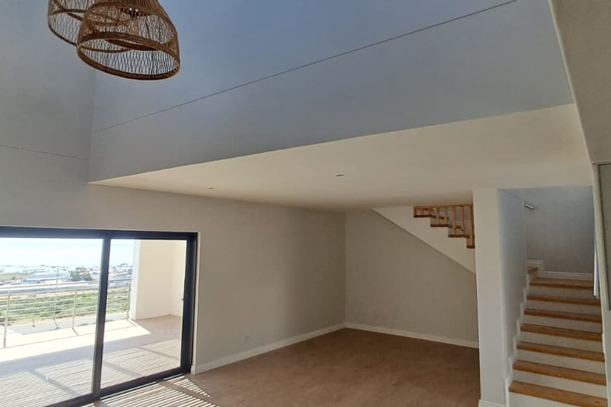 Spacious open-plan living area featuring high ceilings, modern laminate flooring, a staircase, and large sliding glass doors leading to an outdoor balcony.