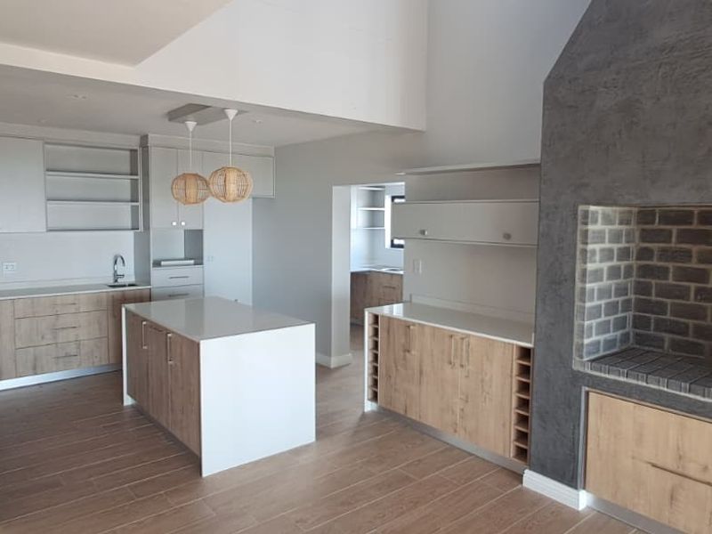 Modern open-plan kitchen featuring a central island, stone countertops, and a prominent built-in indoor braai area with a textured finish.