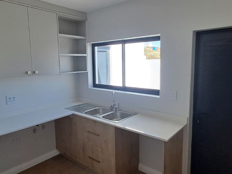 A clean and modern scullery featuring built-in cabinetry, stone countertops, and a double sink with a functional layout.