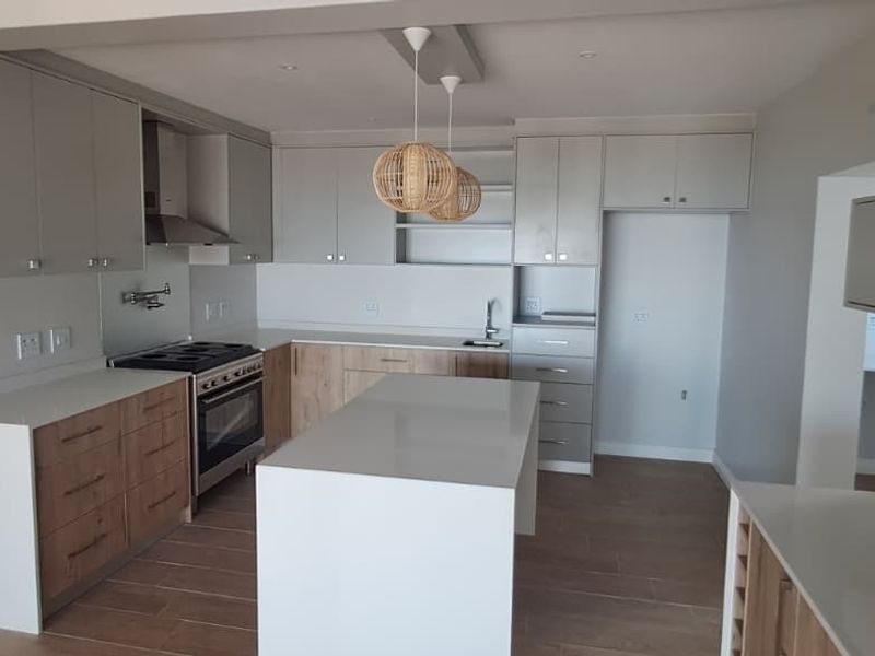 Modern kitchen featuring two-tone cabinetry, a central island with quartz countertops, stainless steel oven, extractor fan, and tiled flooring in an open-plan layout.
