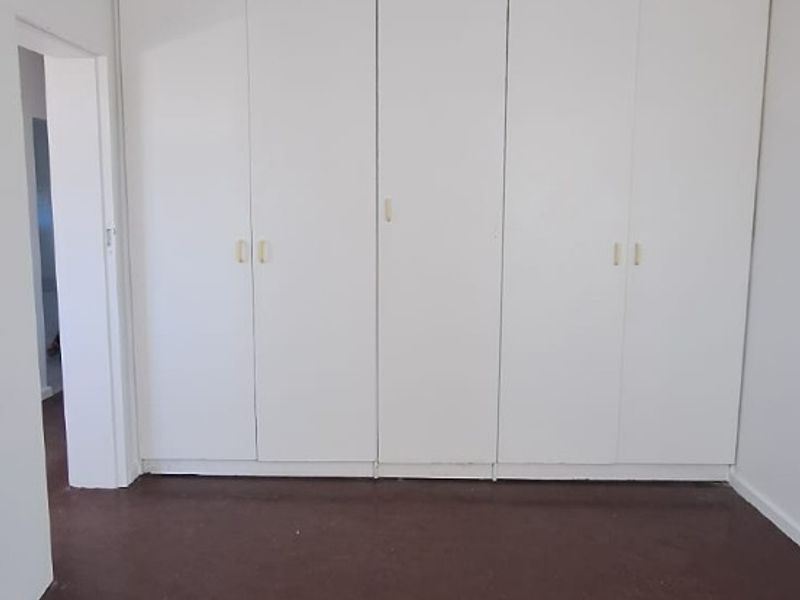 An empty bedroom featuring a wall of built-in cupboards and dark tiled flooring, offering a blank canvas for renovation or interior design.