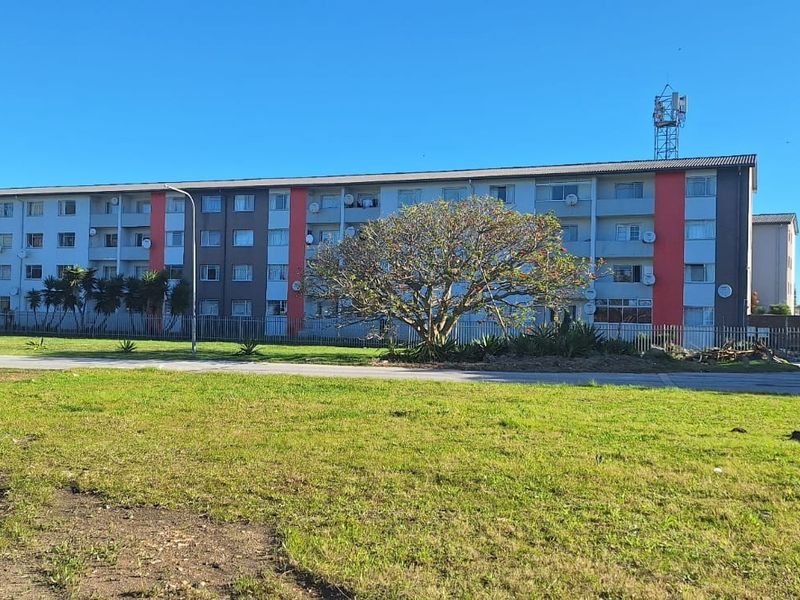 A view of a multi-story apartment building featuring exterior balconies and perimeter fencing, set within a residential complex.