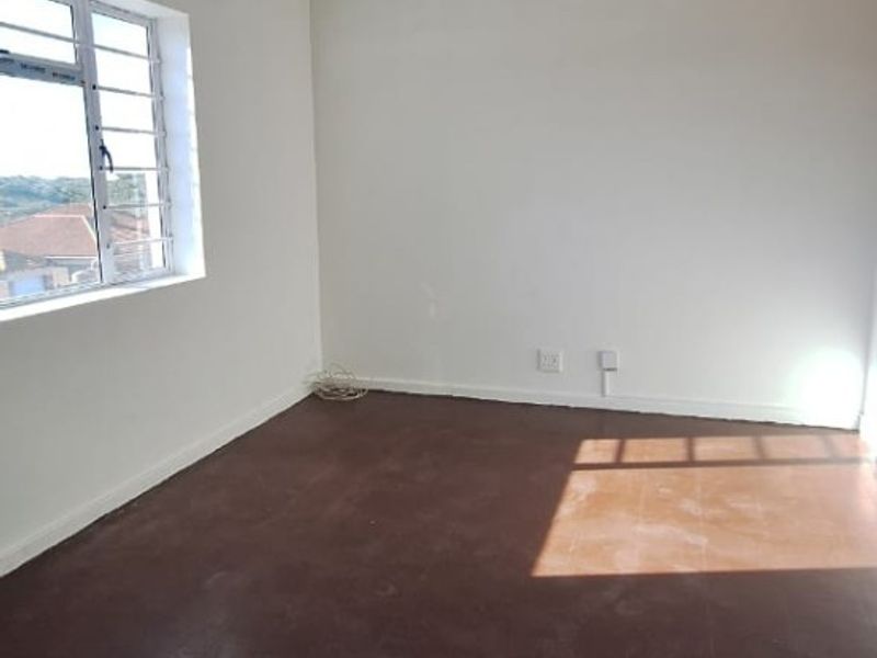 An empty bedroom featuring plain white walls, a window with security bars, and dark flooring, offering a blank canvas for renovation.