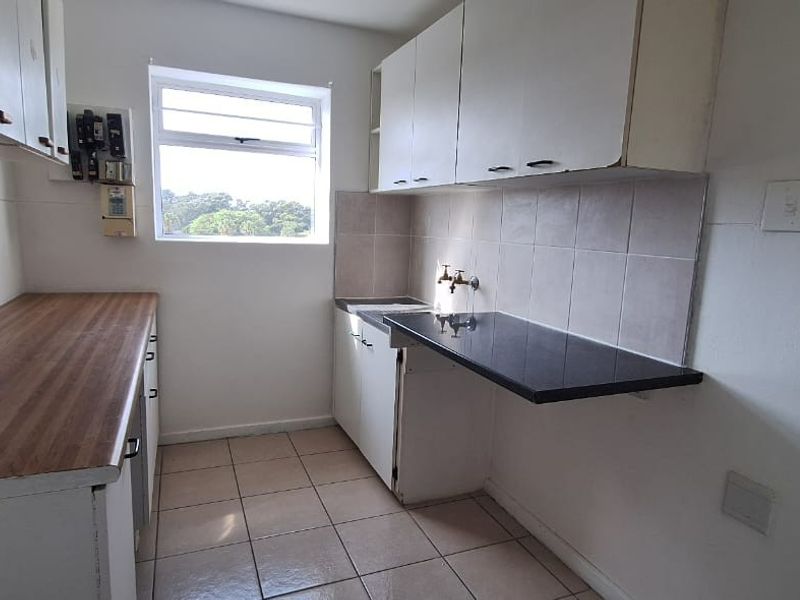 A compact, empty kitchen featuring laminate countertops, tiled backsplash, and basic cabinetry, offering a functional space ready for modernization.