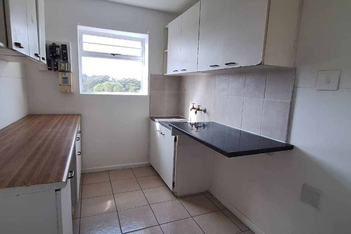 A compact, empty kitchen featuring laminate countertops, tiled backsplash, and basic cabinetry, offering a functional space ready for modernization.