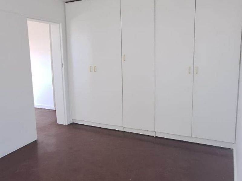 An empty bedroom featuring built-in cupboards and dark tiled flooring, offering a blank canvas for renovation or interior design updates.