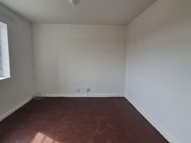 An empty bedroom featuring white walls, an aluminium window frame, and worn flooring, offering a blank canvas for renovation or interior design.
