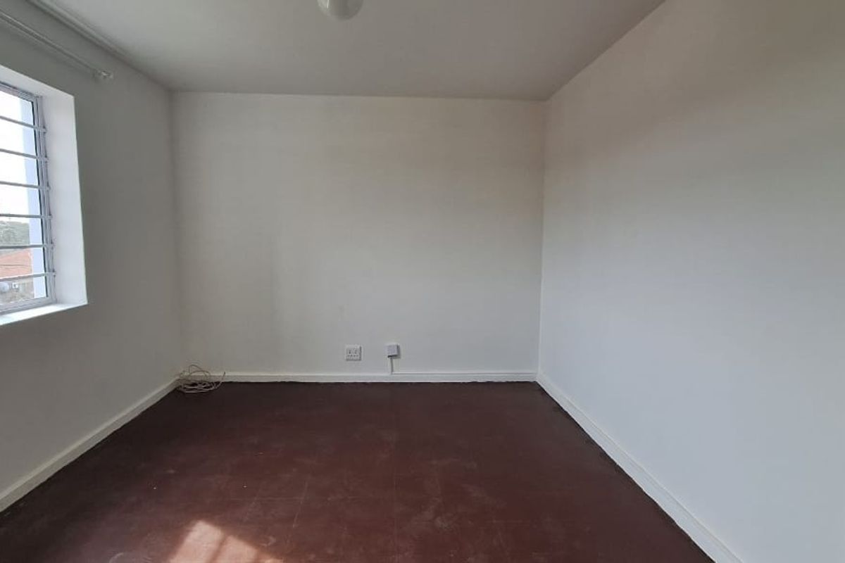 An empty bedroom featuring white walls, an aluminium window frame, and worn flooring, offering a blank canvas for renovation or interior design.