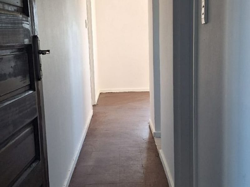 A vacant interior hallway featuring tiled flooring and a timber entrance door, providing access to various rooms within the apartment.