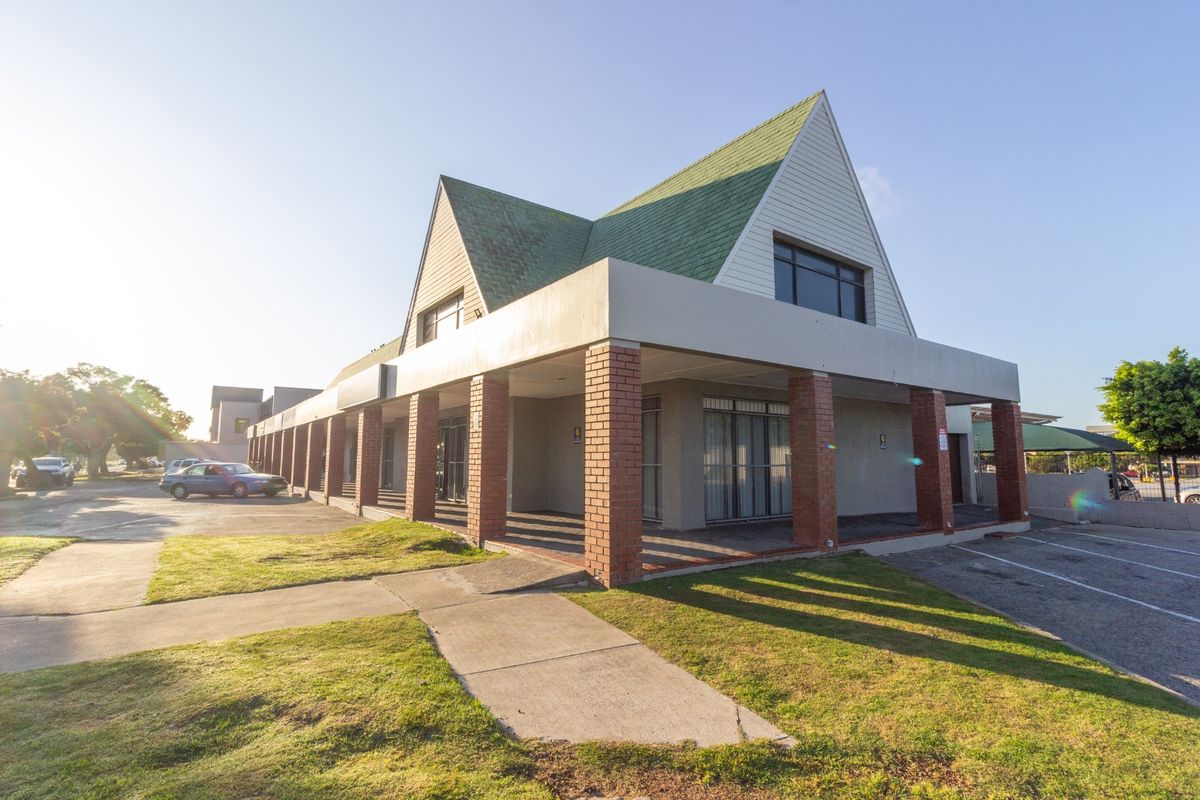 Front exterior view of a retail property featuring a covered walkway with brick columns and a distinctive pitched roof design.